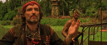 Movie still from “Apocalypse Now” (1979), directed by Francis Ford Coppola – A man with a beard is standing next to another man; Close Up shot, Over the shoulder angle