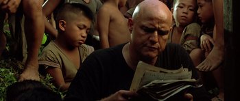 Movie still from “Apocalypse Now” (1979), directed by Francis Ford Coppola – A bald man reading a newspaper while a young boy looks on; Close Up shot, Low angle