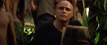 Movie still from “Apocalypse Now” (1979), directed by Francis Ford Coppola – A man with bald head sitting in front of a book; Close Up shot, Low angle