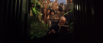 Movie still from “Apocalypse Now” (1979), directed by Francis Ford Coppola – A group of people standing around a man reading a book; Wide shot, High angle