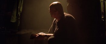 Movie still from “Apocalypse Now” (1979), directed by Francis Ford Coppola – A bald man sitting in a dark room with a cell phone in his hand; Medium shot, Low angle