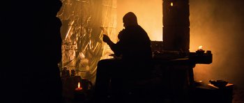 Movie still from “Apocalypse Now” (1979), directed by Francis Ford Coppola – A man sitting in front of a fire holding a cigarette; Medium shot, Low angle