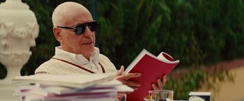 Movie still from “Argo” (2012), directed by Ben Affleck – An older man reading a book while sitting at a table; Close Up shot, Over the shoulder angle