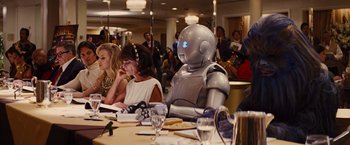 Movie still from “Argo” (2012), directed by Ben Affleck – People sitting at a table in a room with a robot; Medium shot, Over the shoulder angle