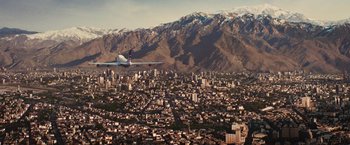 Movie still from “Argo” (2012), directed by Ben Affleck – An airplane flying over a city with mountains in the background; Extreme Wide shot, High angle