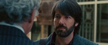 Movie still from “Argo” (2012), directed by Ben Affleck – A man with long hair and a beard is talking to another man; Close Up shot, Over the shoulder angle