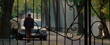 Movie still from “Argo” (2012), directed by Ben Affleck – A car parked on the side of the road behind a gate; Wide shot, Over the shoulder angle
