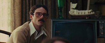 Movie still from “Argo” (2012), directed by Ben Affleck – A man with a mustache wearing glasses and a sweater; Close Up shot, Over the shoulder angle