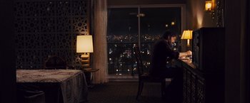Movie still from “Argo” (2012), directed by Ben Affleck – A man sitting at a table in front of a large window; Wide shot, High angle