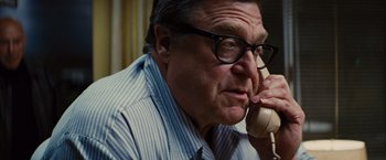 Movie still from “Argo” (2012), directed by Ben Affleck – An older man talking on a phone while wearing glasses; Close Up shot, Over the shoulder angle