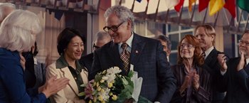 Movie still from “Argo” (2012), directed by Ben Affleck – An older man holding a bouquet of flowers while standing next to an older woman; Medium shot, Over the shoulder angle