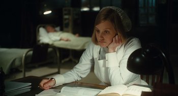 Movie still from “Atonement” (2007), directed by Joe Wright – A woman in white shirt sitting at a table with a book; Medium shot, High angle
