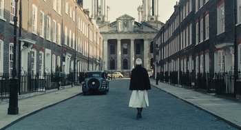 Movie still from “Atonement” (2007), directed by Joe Wright – A woman is walking down the street in front of an old car; Extreme Wide shot, Low angle