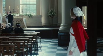 A woman dressed as a nun stands in front of chairs in an empty room