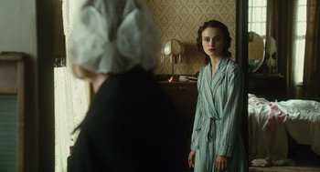 Movie still from “Atonement” (2007), directed by Joe Wright – A woman standing in front of a mirror in a room; Medium shot, Over the shoulder angle