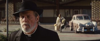 Movie still from “Bad Times at the El Royale” (2018), directed by Drew Goddard – An old man wearing a priest's outfit and a hat; Close Up shot, Over the shoulder angle