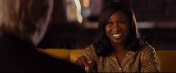 Movie still from “Bad Times at the El Royale” (2018), directed by Drew Goddard – A woman sitting on a couch smiling for the camera; Close Up shot, Over the shoulder angle