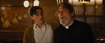 Movie still from “Bad Times at the El Royale” (2018), directed by Drew Goddard – A man standing next to another man wearing a priest's outfit; Medium shot, Low angle