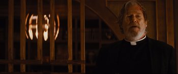 Movie still from “Bad Times at the El Royale” (2018), directed by Drew Goddard – A man sitting in front of a bookshelf in a dark room; Close Up shot, Over the shoulder angle