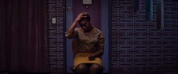 Movie still from “Bad Times at the El Royale” (2018), directed by Drew Goddard – A woman sitting on a chair with her hand on her head; Medium shot, High angle