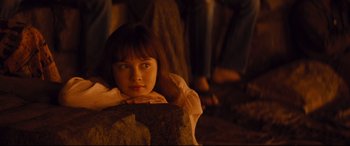 Movie still from “Bad Times at the El Royale” (2018), directed by Drew Goddard – A young girl sitting on top of a rock in front of a group of people; Medium shot, High angle