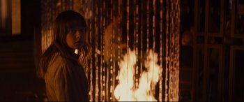 Movie still from “Bad Times at the El Royale” (2018), directed by Drew Goddard – A woman standing in front of a fire pit; Medium shot, Over the shoulder angle