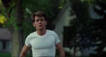 Movie still from “Badlands” (1973), directed by Terrence Malick – A man in a white t - shirt is standing in front of a house; Medium shot, Low angle