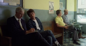 Movie still from “Badlands” (1973), directed by Terrence Malick – A group of men sitting on a bench in a room; Medium shot, Over the shoulder angle