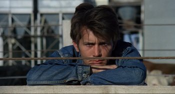 Movie still from “Badlands” (1973), directed by Terrence Malick – A young man leaning on a fence looking sad; Close Up shot, Over the shoulder angle