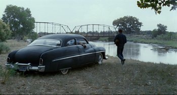 Movie still from “Badlands” (1973), directed by Terrence Malick – An old car parked next to a river; Wide shot, Over the shoulder angle