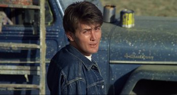 Movie still from “Badlands” (1973), directed by Terrence Malick – A man in a denim jacket standing in front of a truck; Close Up shot, Over the shoulder angle