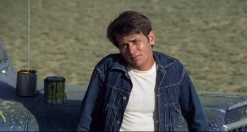 Movie still from “Badlands” (1973), directed by Terrence Malick – A young man in a jean jacket is sitting on a park bench; Close Up shot, High angle