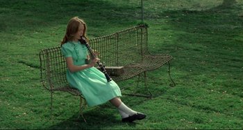 Movie still from “Badlands” (1973), directed by Terrence Malick – A young girl sitting on a bench playing a violin; Wide shot, High angle