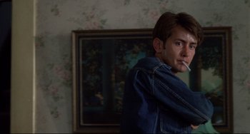Movie still from “Badlands” (1973), directed by Terrence Malick – A man smoking a cigarette in front of a painting; Medium shot, Over the shoulder angle