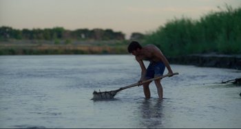 Movie still from “Badlands” (1973), directed by Terrence Malick – A young man in the middle of a body of water holding a wooden stick; Wide shot, Low angle