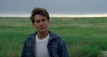 Movie still from “Badlands” (1973), directed by Terrence Malick – A man in a denim jacket standing in a grassy field; Close Up shot, Over the shoulder angle