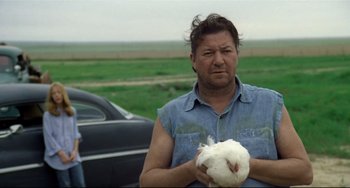 Movie still from “Badlands” (1973), directed by Terrence Malick – A man holding a chicken in front of a black car; Close Up shot, High angle