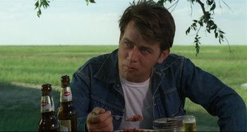 Movie still from “Badlands” (1973), directed by Terrence Malick – A man sitting at a picnic table eating food; Close Up shot, Over the shoulder angle