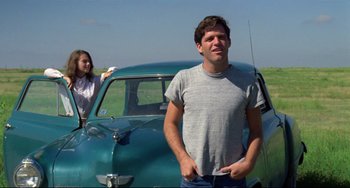 Movie still from “Badlands” (1973), directed by Terrence Malick – A man standing next to an old blue car; Medium shot, Low angle
