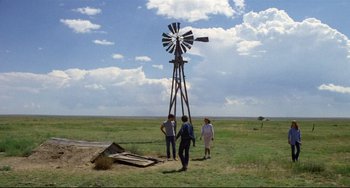 Movie still from “Badlands” (1973), directed by Terrence Malick – A group of people standing in a field next to a windmill; Wide shot, Over the shoulder angle