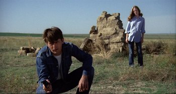 Movie still from “Badlands” (1973), directed by Terrence Malick – A man kneeling down next to a woman in a field; Wide shot, Low angle