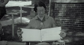 Movie still from “Badlands” (1973), directed by Terrence Malick – An older woman holding an open book in front of a brick building; Medium shot, Low angle