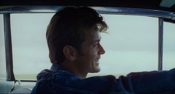 Movie still from “Badlands” (1973), directed by Terrence Malick – A man in a blue jean jacket driving a car; Close Up shot, Over the shoulder angle