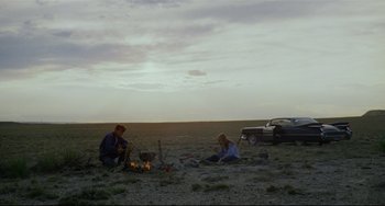 Movie still from “Badlands” (1973), directed by Terrence Malick – Two people sitting around a fire in a field; Extreme Wide shot, Low angle