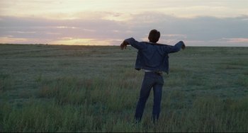 Movie still from “Badlands” (1973), directed by Terrence Malick – A man standing in a field with his arms outstretched; Wide shot, Over the shoulder angle