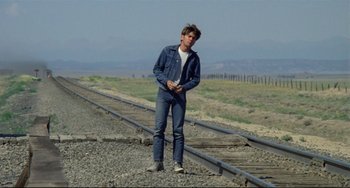 Movie still from “Badlands” (1973), directed by Terrence Malick – A young man standing on the side of a train track; Wide shot, Low angle