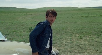 Movie still from “Badlands” (1973), directed by Terrence Malick – A man standing next to a car in a grassy field; Medium shot, Over the shoulder angle