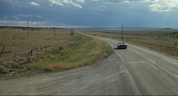 Movie still from “Badlands” (1973), directed by Terrence Malick – A car driving down a road in the middle of a field; Extreme Wide shot, High angle