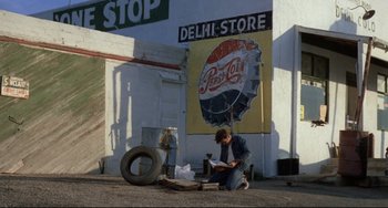 Movie still from “Badlands” (1973), directed by Terrence Malick – A man sitting on the ground reading a newspaper; Wide shot, Low angle