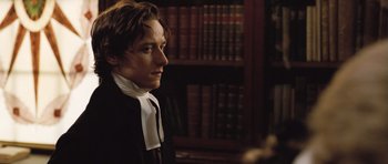 Movie still from “Becoming Jane” (2007), directed by Julian Jarrold – A man in a suit and tie in front of a book shelf; Close Up shot, Over the shoulder angle